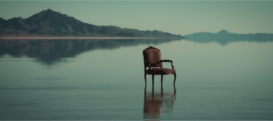 A single chair in the middle of a serene lake with mountains in the background.